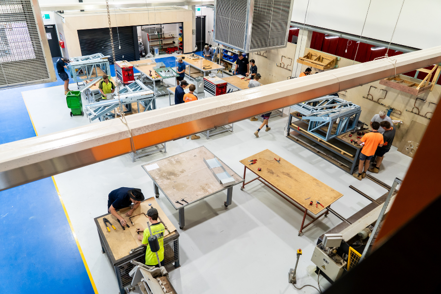 Overhead view of a busy workshop with several individuals in hi-vis wear working on various construction projects involving wood and metal.