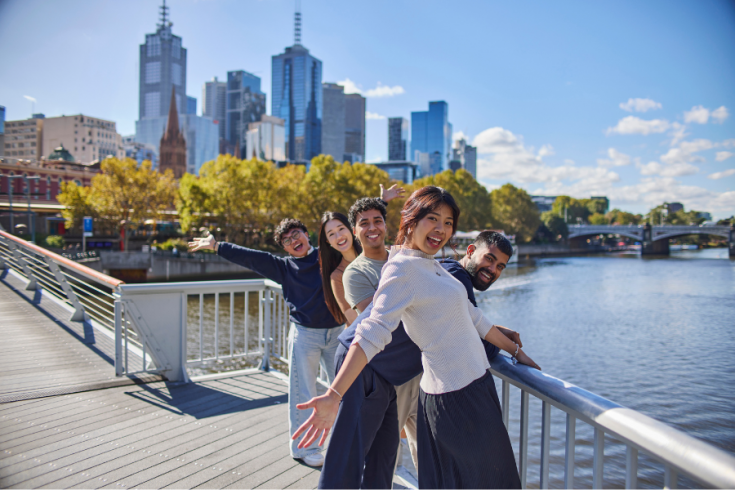 Students leaning on footbridge over the yarra river with Melbourne CBD in background