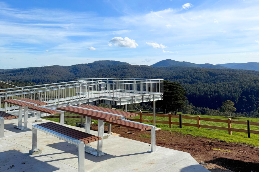 Viewing platform and benches overlooking a scenic landscape with lush green mountains under a blue sky.