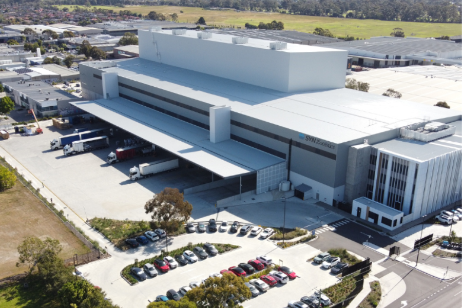 Aerial view of the Synnex Oceana facility in Oakleigh South with multiple sections, a wide parking area with numerous vehicles, and several trucks parked at loading bays.