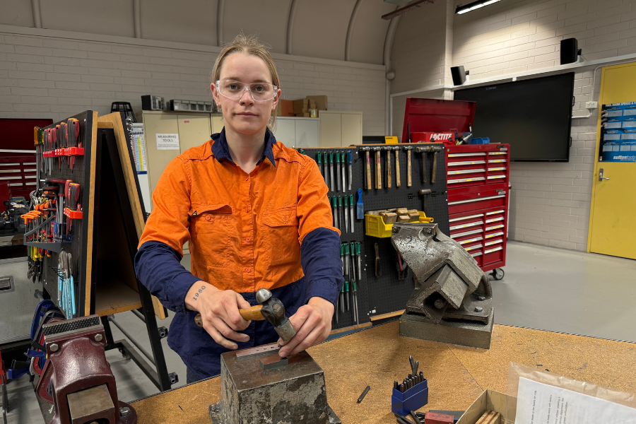 Madi in high-vis wear working in workshop holding a hammer