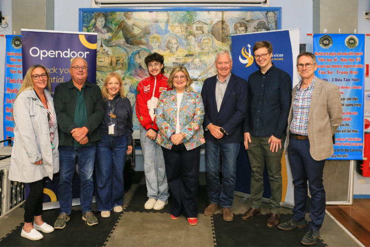 A group of 8 people standing in front of a mural and banners for the Western Pathways Program.