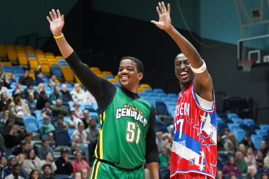 Two basketball players from Washington Generals and Harlem Globetrotters waving to fans from a basketball court 