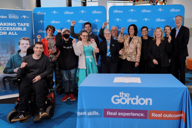 A group of people pose together at an event. They stand in front of a backdrop that reads 