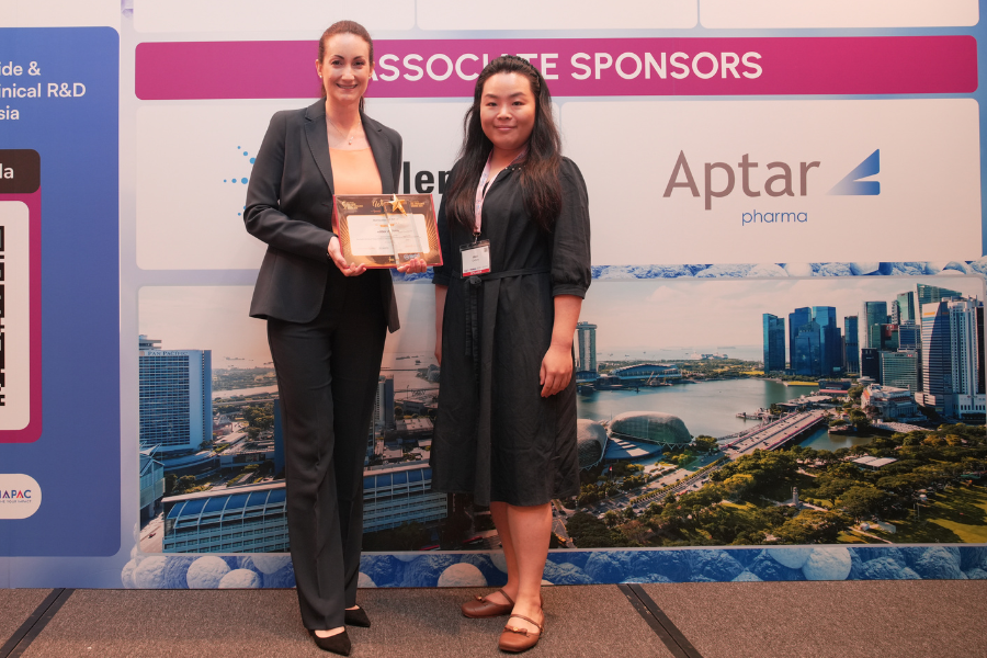 Two people smiling at the camera, one is holding an award