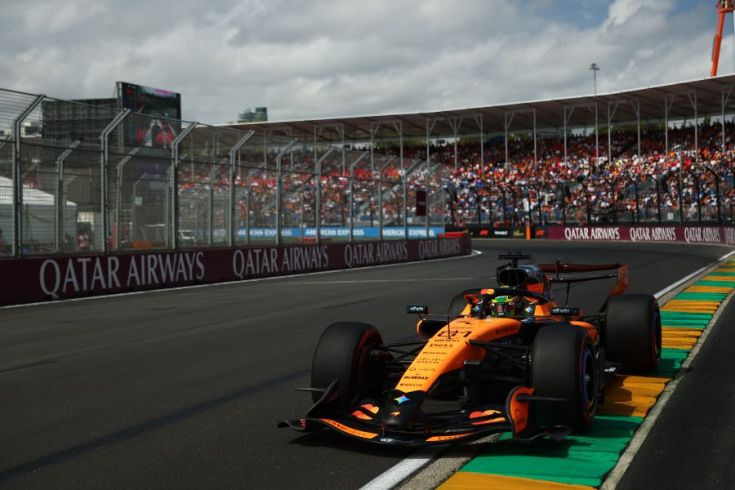 A Formula 1 car is driving on a track. Large crowds and fences are in the background.