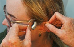 Two hands placing a hearing aid into the ear of a woman
