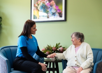 Diana Pasos in a blue uniform sitting across a small table from an elderly person.