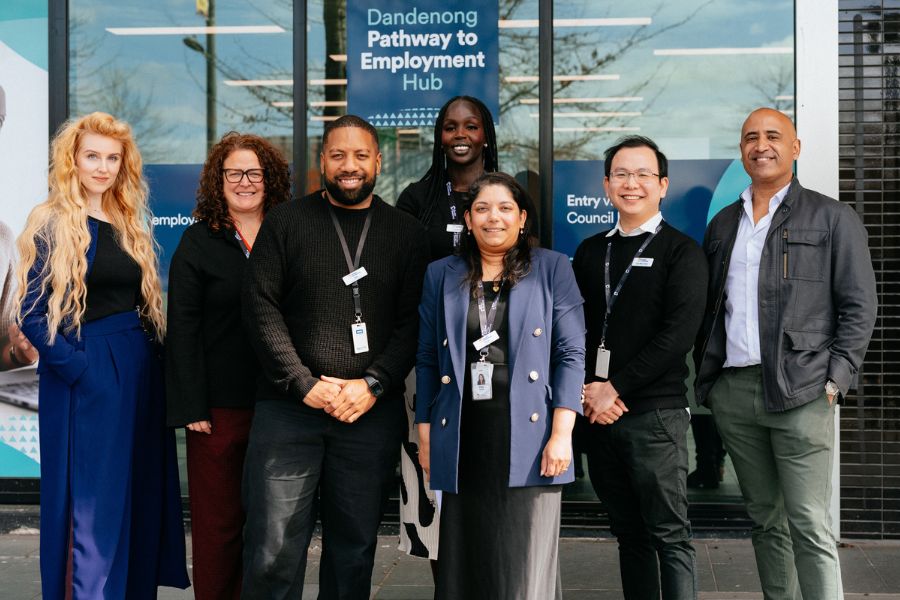 Seven people smile and pose for the camera outside the Dandenong Pathway to Employment Hub