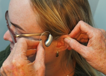 Two hands placing a hearing aid into the ear of a woman