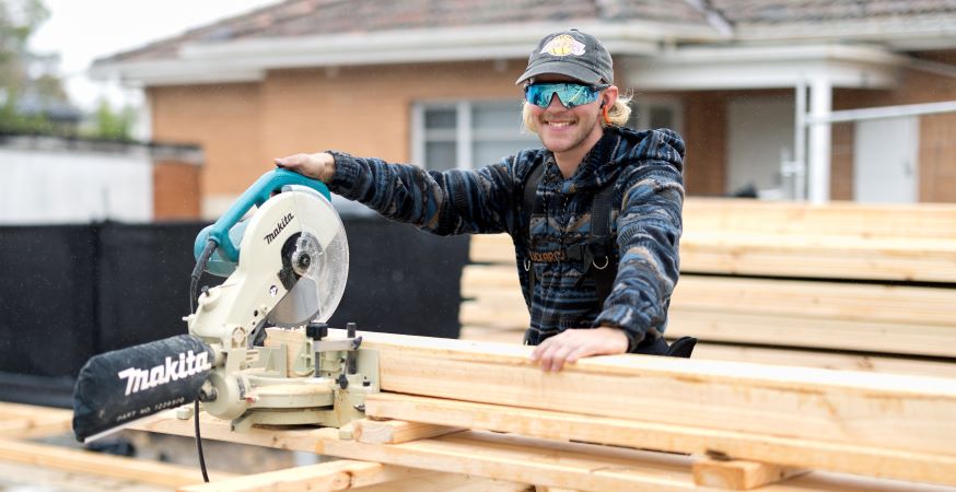 Jack Kelsey with a power saw and timber in front of a house he's building