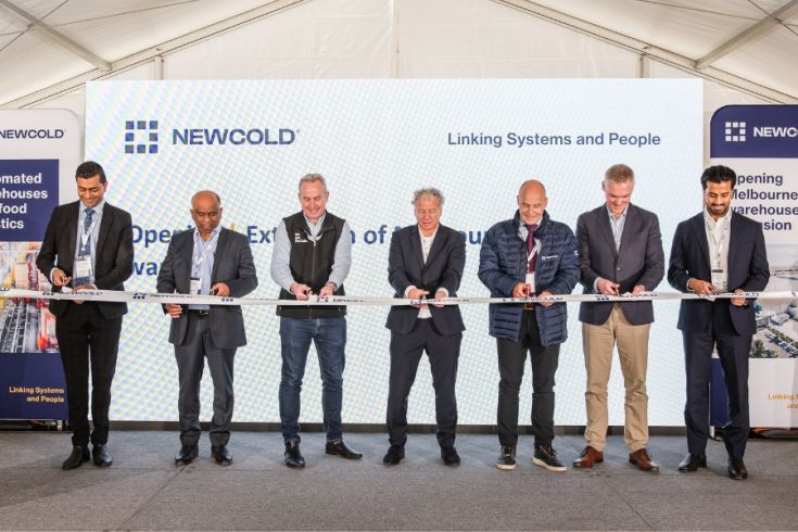 Seven people stand in front of a backdrop with NewCold logo, smiling and holding a white ribbon, suggesting a ribbon-cutting ceremony. 